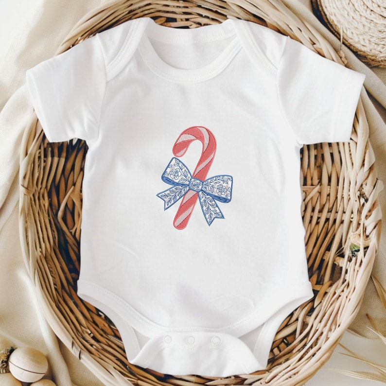 May include: A white short-sleeved baby bodysuit featuring a central embroidered graphic of a red and white striped candy cane tied with a blue and white floral patterned bow. The garment has a round neckline and snap closures at the bottom.