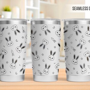 May include: Three white stainless steel tumblers with a seamless design featuring a repeating pattern of black and white bunny rabbits and carrots. The tumblers are all the same size and shape.