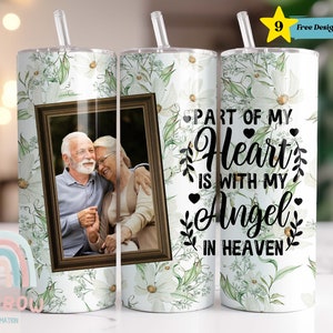 May include: White stainless steel tumbler with a floral design and a photo frame. The photo frame contains a picture of an older couple. The tumbler has the text "Part of my heart is with my angel in heaven" printed on it.