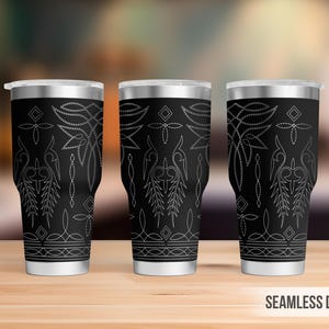 May include: Three black insulated tumblers with silver lids and a decorative white embroidered design. The design features floral and geometric patterns. The tumblers are displayed on a wooden surface.