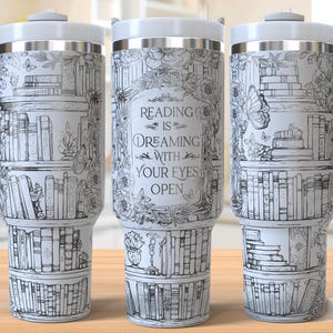May include: White travel mug featuring a black and white illustration of bookshelves, butterflies, and floral designs. The mug has a white handle and lid, and the text "Reading is Dreaming with Your Eyes Open."