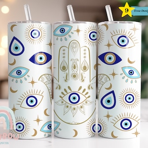 Op de afbeelding: Drie witte roestvrijstalen bekers met een blauw en gouden boze oog ontwerp. De bekers hebben een rietje en een deksel. De bekers staan op een wit oppervlak. 9 Gratis Ontwerpen Inbegrepen.