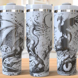 Puede incluir: Tres tazas de viaje de acero inoxidable con diseños de dragones en blanco y negro. Las tazas tienen un fondo blanco con ilustraciones de dragones negros. Las tazas tienen un asa en el lateral y una tapa en la parte superior.