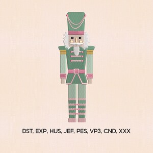 May include: An embroidered design of a green and pink nutcracker soldier. The nutcracker has a tall hat, a white beard, and is wearing a uniform with gold accents. The text "DST, EXP, HUS, JEF, PES, VP3, CND, XXX" is at the bottom.