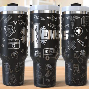 Puede incluir: Taza de viaje de acero inoxidable negro con un diseño blanco de símbolos médicos, incluyendo un caduceo, una estrella de la vida, un botiquín de primeros auxilios y la palabra "EMS".