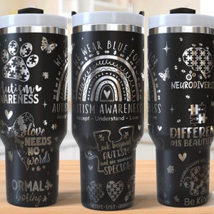 May include: Three black stainless steel travel mugs with silver designs. The mugs feature various designs related to autism awareness, including puzzle pieces, rainbows, and the text "We Wear Blue For Autism Awareness".