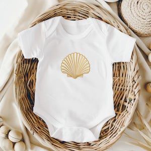 May include: White baby onesie with a gold seashell design. The short-sleeved bodysuit is made of soft material and features a snap closure. The seashell is centered on the front of the onesie. The onesie is displayed in a woven basket.