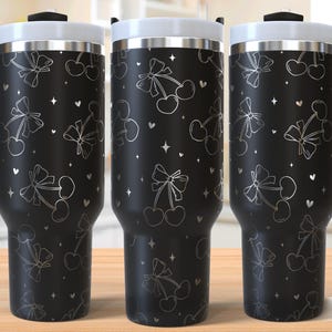 May include: Black stainless steel travel mug with a white design of cherries and bows. The mug has a handle and a lid.
