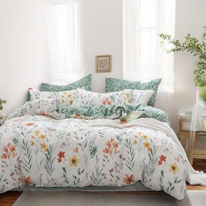 May include: A white duvet cover with a floral pattern featuring green leaves, yellow, orange, and red flowers. The duvet cover is on a bed with green and white patterned pillowcases.