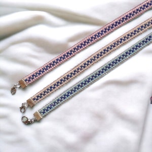 Puede incluir: Tres pulseras de cuentas con cierres plateados. Las pulseras están hechas con cuentas rosas, beige y azul claro con detalles en azul oscuro.