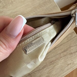 May include: A tan leather handbag with a zipper closure. The interior is lined with a patterned fabric. A metal tag inside the bag reads "LE TANNEUR DEPUIS 1898".
