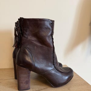 May include: A pair of brown leather ankle boots with wooden block heels. The boots have a rounded toe and a zipper detail on the back. The heels are approximately 3 inches tall.