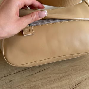 May include: A tan shoulder bag with a rectangular shape. The bag has a zipper closure and a matching strap. The bag is made of a smooth material and has a minimalist design.
