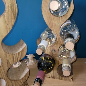 May include: Wooden wine rack with a unique, abstract design. The rack is made of natural wood and has a rustic finish. It can hold up to six bottles of wine.