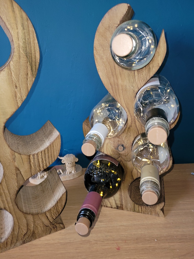 May include: Wooden wine rack with a unique, abstract design. The rack is made of natural wood and has a rustic finish. It can hold up to six bottles of wine.