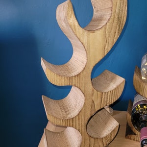May include: Wooden wine rack shaped like a tree with five bottle holders. The rack is made of light brown wood and has a natural finish.