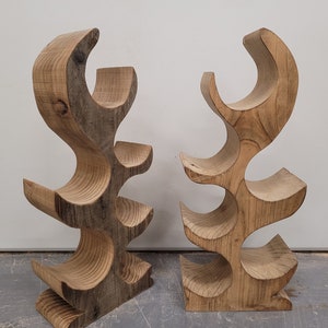 May include: Two wooden wine bottle holders, each with a unique, organic shape and five bottle slots. The holders are made of natural wood with a rustic finish.