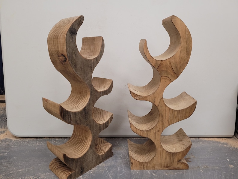 May include: Two wooden wine bottle holders, each with a unique, organic shape and five bottle slots. The holders are made of natural wood with a rustic finish.