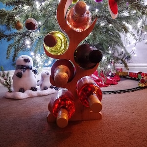 May include: Wooden wine rack shaped like a tree branch with five bottles of wine. The rack is decorated with a red and white Christmas ornament and is sitting under a Christmas tree.