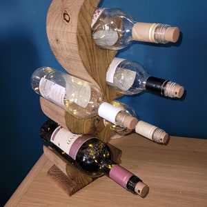 May include: A wooden wine rack with a unique, curved design. The rack holds four bottles of wine, two white and two red. The rack is made of natural wood and has a rustic look.