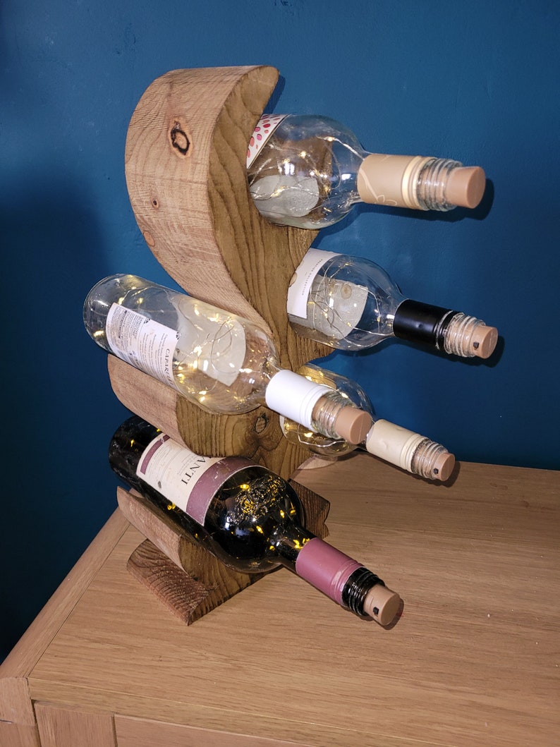 May include: A wooden wine rack with a unique, curved design. The rack holds four bottles of wine, two white and two red. The rack is made of natural wood and has a rustic look.
