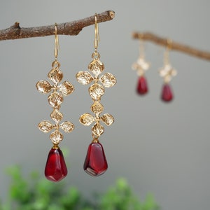 May include: Gold earrings with a floral design and red teardrop-shaped stones.