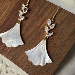 May include: A pair of gold earrings with a white shell fan-shaped pendant and a crystal leaf design.