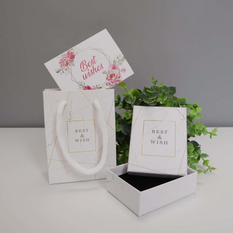 May include: A white gift bag and a matching square gift box, both featuring a marble pattern with gold geometric lines and the text Best & Wish. A rectangular card with pink roses and the text Best wishes is tucked inside the gift bag.