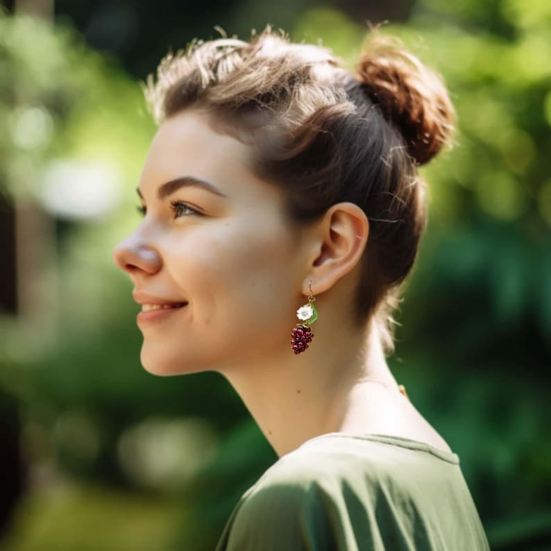 Op de afbeelding: Een vrouw met bruin haar draagt een groen shirt en oorbellen met een witte bloem en een tros rode bessen.