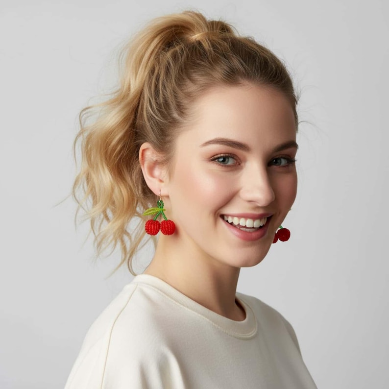 May include: A woman wearing red cherry earrings with green leaves. The earrings are a fun, playful accessory, perfect for adding a pop of color to any outfit. The earrings are a unique and eye-catching piece of jewelry.