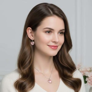 May include: A silver necklace and matching drop earrings set featuring light pink heart-shaped pendants. The necklace has a delicate silver chain with a single heart charm, while the earrings consist of small silver hoops with heart drops.