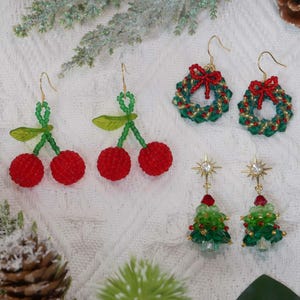 May include: A collection of beaded earrings in festive designs. Includes cherry, wreath, and Christmas tree shapes. The earrings feature red, green, and gold beads with gold-colored hooks. Perfect for holiday or seasonal wear.