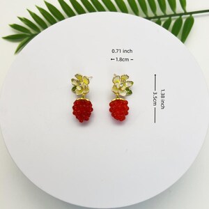 May include: A pair of gold earrings with a red and white flower design. The earrings are 1.38 inches long and 0.71 inches wide.