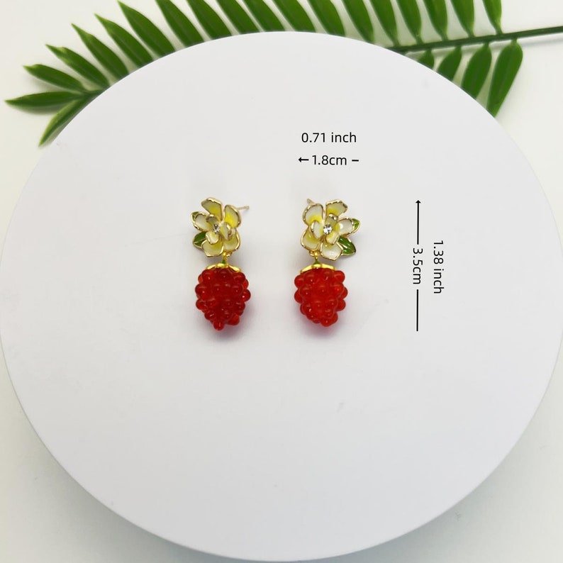 May include: A pair of gold earrings with a red and white flower design. The earrings are 1.38 inches long and 0.71 inches wide.