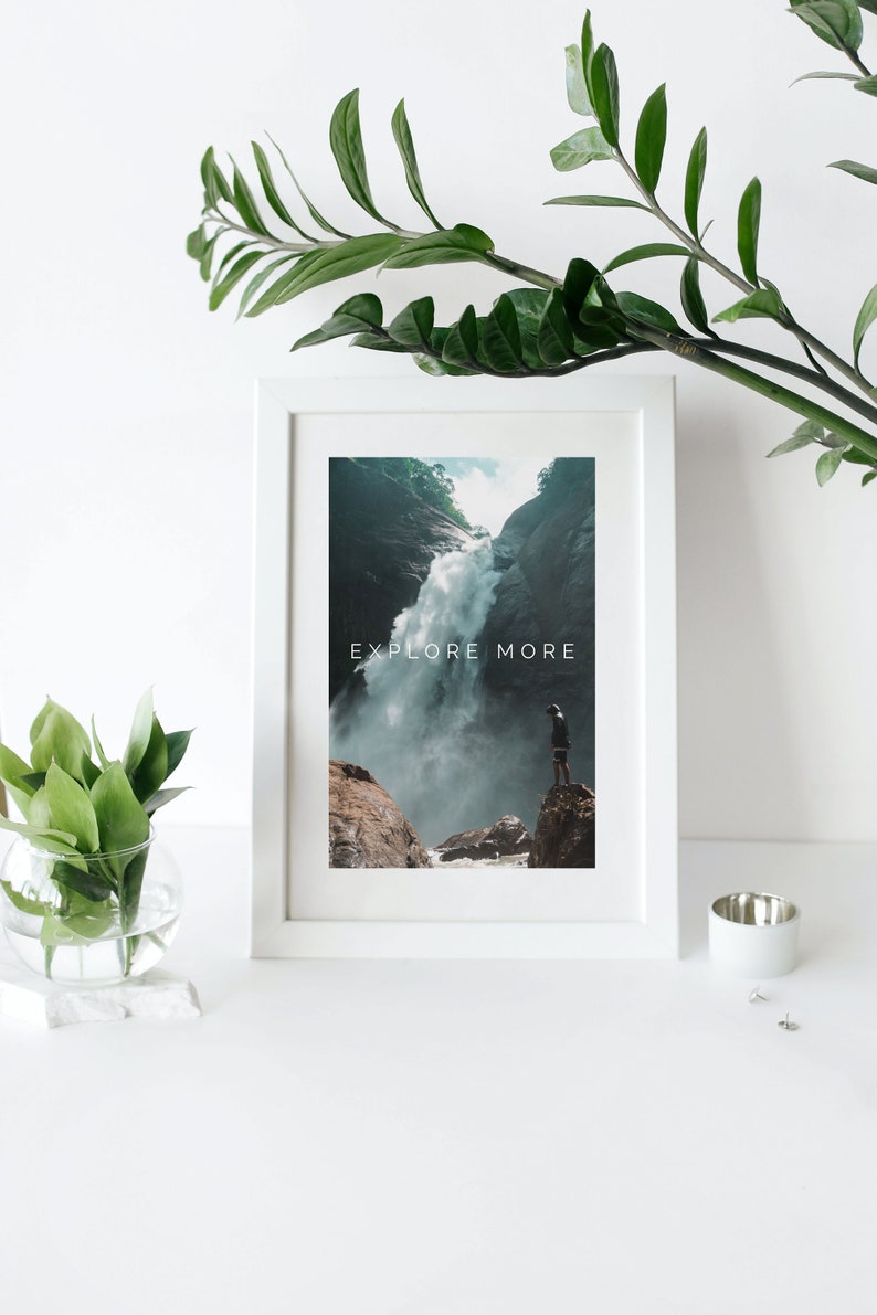 Peut inclure: Une impression encadr&eacute;e blanche avec une photographie d'une cascade dans une for&ecirc;t luxuriante et verte. Le texte "EXPLORE MORE" est imprim&eacute; en blanc sur l'image.