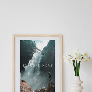 Peut inclure: Une impression encadr&eacute;e avec une photographie d'une cascade dans une for&ecirc;t luxuriante et verte. Le texte "EXPLORE MORE" est imprim&eacute; en blanc sur l'image. Une personne se tient sur un rocher surplombant la cascade.
