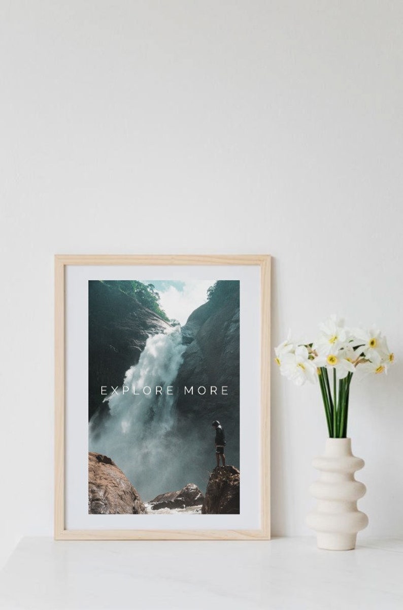 Peut inclure: Une impression encadr&eacute;e avec une photographie d'une cascade dans une for&ecirc;t luxuriante et verte. Le texte "EXPLORE MORE" est imprim&eacute; en blanc sur l'image. Une personne se tient sur un rocher surplombant la cascade.
