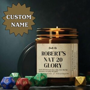May include: A brown glass candle jar with a lit wick, labeled "ROBERT'S NAT 20 GLORY." The label includes text about dice rolls. Various polyhedral dice in blue, red, green, and gold surround the candle, suggesting a gaming theme.