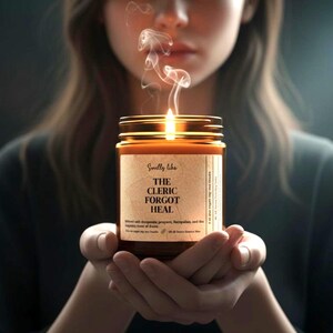May include: A lit candle in a glass jar with a gold lid, held in cupped hands. The candle's label reads "Smells like The Cleric Forgot Heal." Smoke rises from the flame. The background is dark with blurred lights.