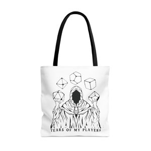 May include: A white tote bag with black handles and a black and white illustration of a hooded figure surrounded by dice. The text "TEARS OF MY PLAYERS" is printed below the figure.