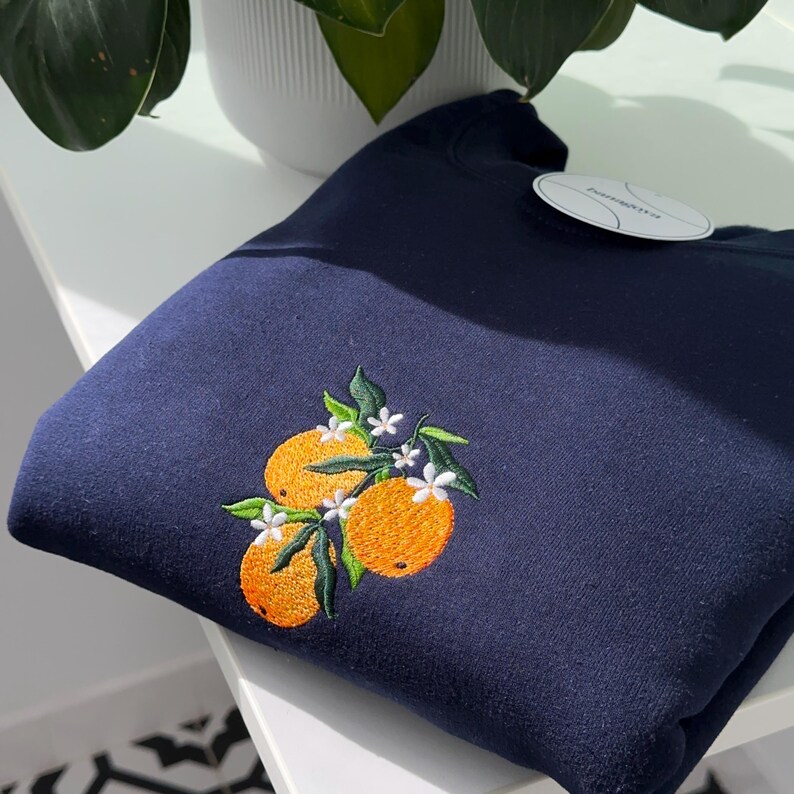 May include: A navy blue sweatshirt with an embroidered design of three oranges with white flowers and green leaves.