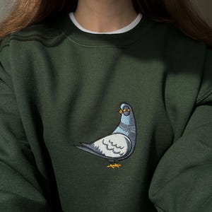 embroidered pigeon on dark green sweatshirt, minimalist bird design on chest, funny pigeon shirt aesthetic, casual unisex outfit