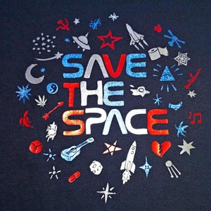 Può includere: Una maglietta blu scuro con un design grafico bianco, rosso e blu che dice "Save the Space". Il grafico è circondato da vari simboli, tra cui stelle, razzi e una chitarra.
