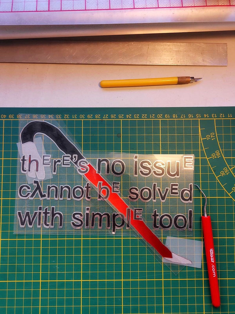 May include: A red and black vinyl sticker with the text "there's no issue cannot be solved with simple tool" on a green cutting mat.