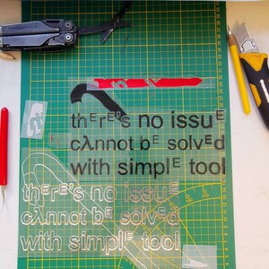 May include: A green cutting mat with a white stencil on top. The stencil has the text "there's no issue that cannot be solved with simple tools" repeated twice. The text is in black and the background of the stencil is white.