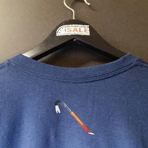 May include: A navy blue t-shirt with an embroidered crowbar design. The t-shirt is hanging on a black hanger with a white tag that says "Doomsday Sale" and "DoomsdaySaleEtsy.com".