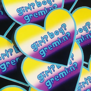 May include: A heart-shaped sticker with a yellow, white, purple, and black gradient. The sticker has the text "girl? boy? gremlin?" in blue letters.