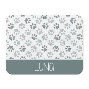May include: A white rectangular pet mat with a light blue paw print pattern and a dark blue band at the bottom with the name "LUNA" written in white.