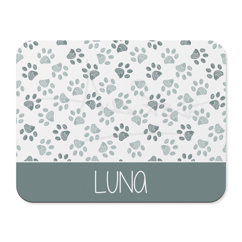 May include: A white rectangular pet mat with a light blue paw print pattern and a dark blue band at the bottom with the name "LUNA" written in white.