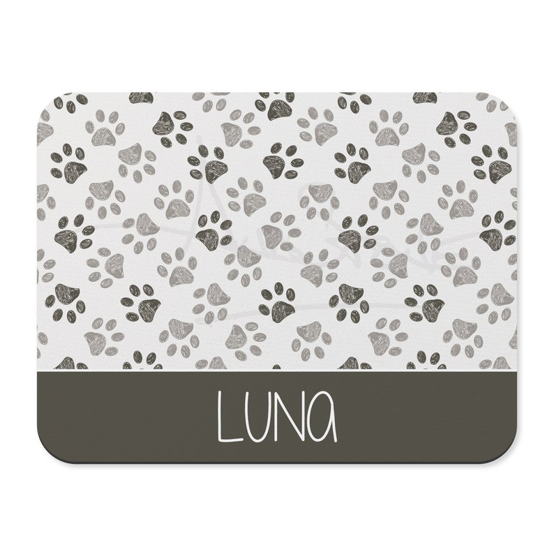May include: A white rectangular pet mat with a gray paw print pattern and a dark gray border. The name "LUNA" is printed in white on the border.
